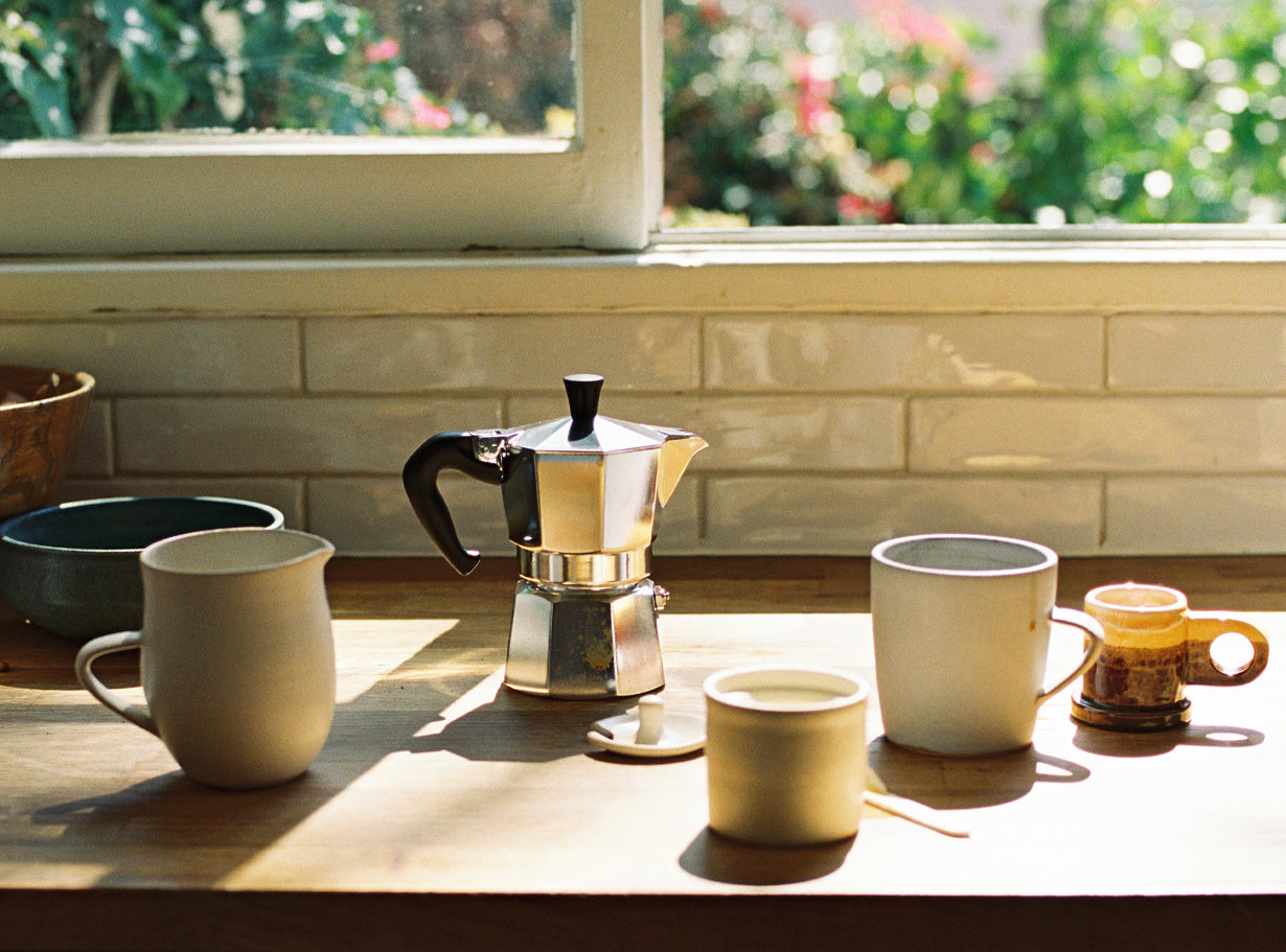 Ceramic mugs and a mokapot for coffee on a wooden counter